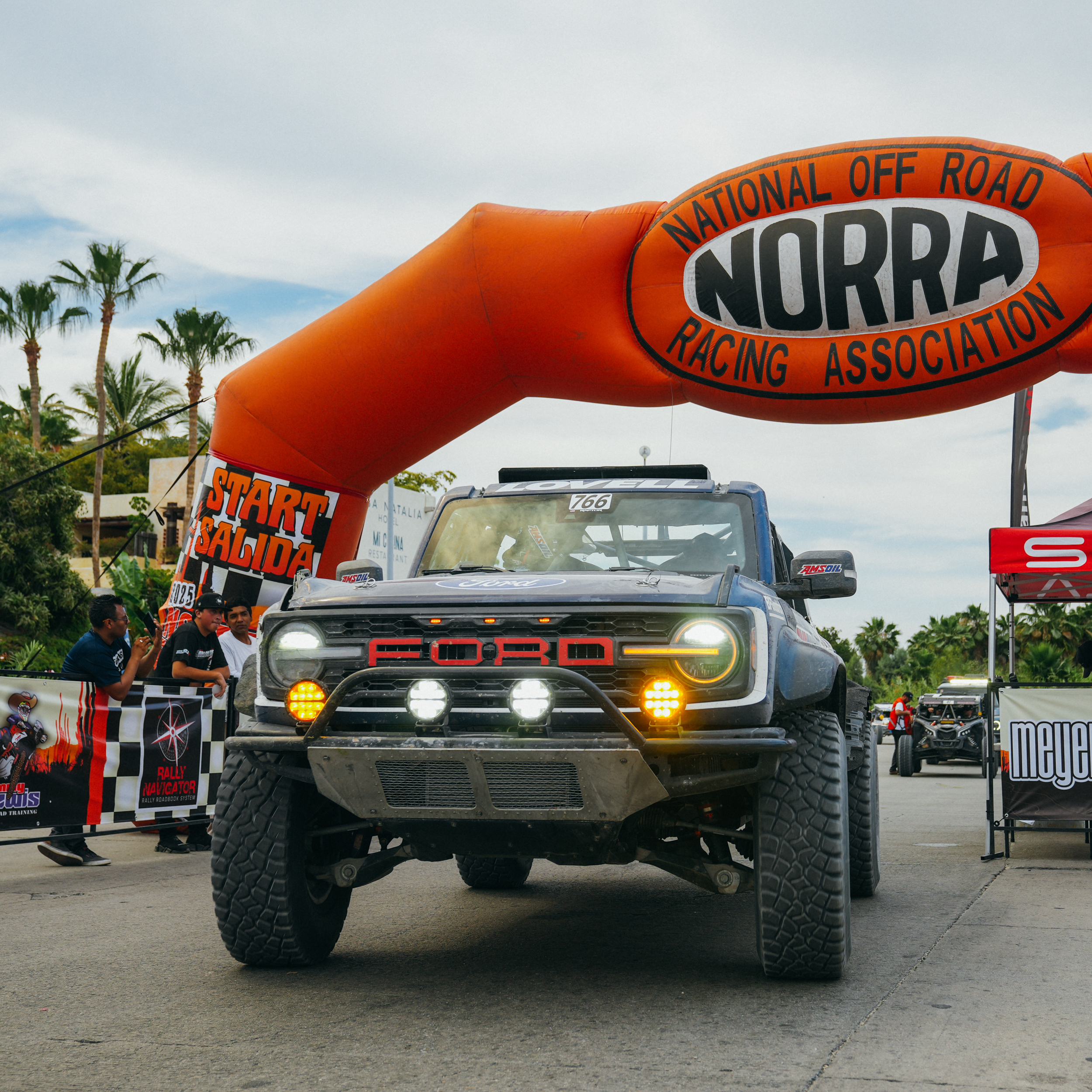 A Bronco Raptor driving beneath the 2025 NORRA Mexican 1000 banner.
